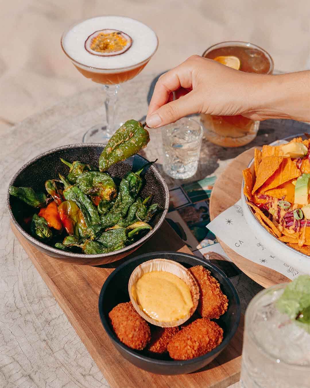 Borrel op tafel met cocktails, padron pepers, nachos en rendangkroketjes