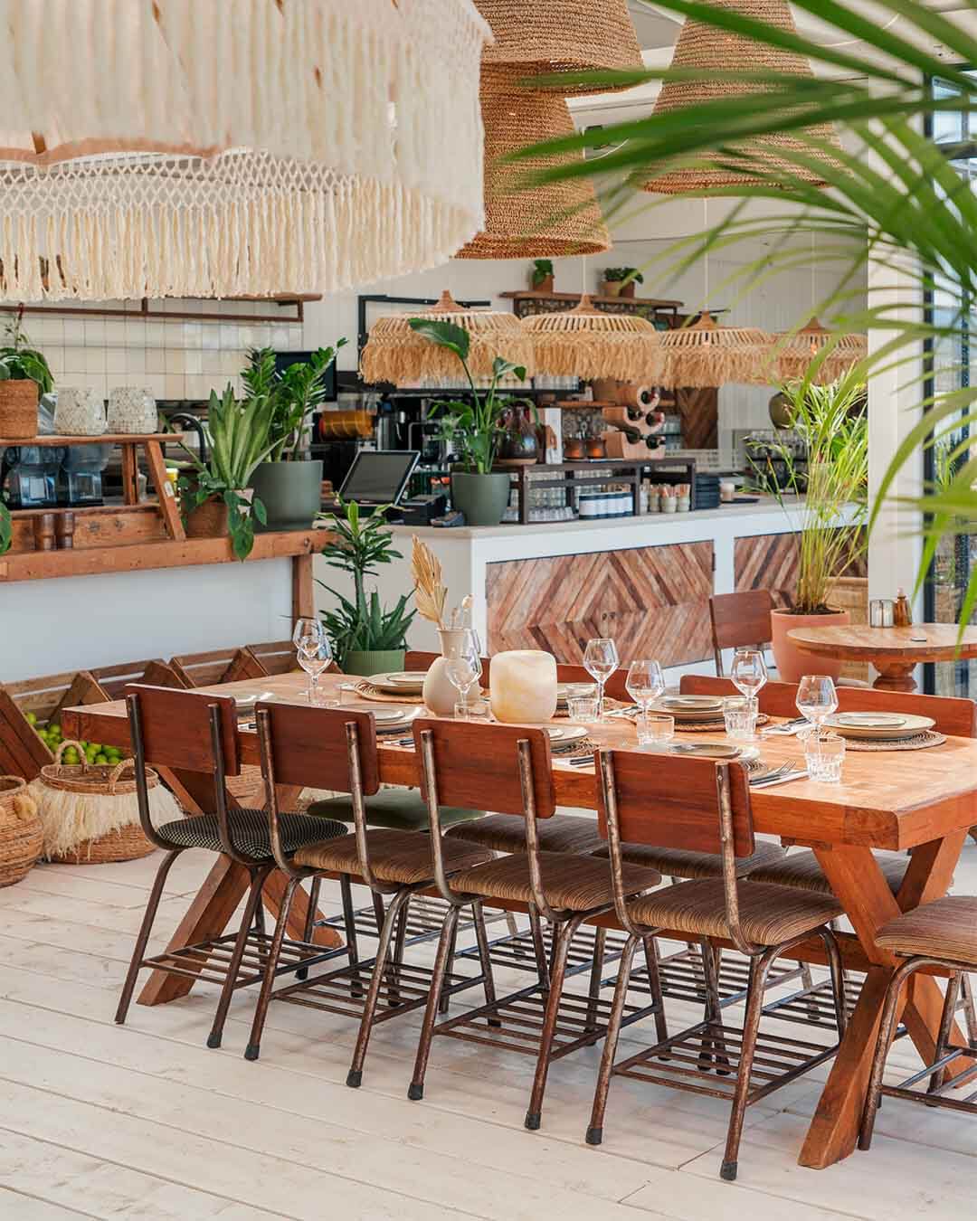 Ingedekte groten teakhouten tafel binnen voor de bar bij hotspot Tulum in Noordwijk