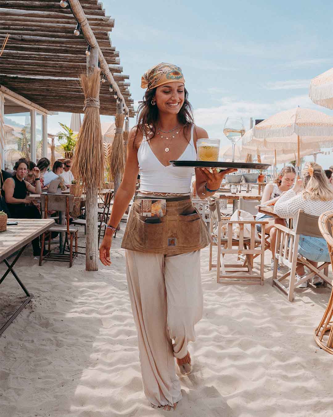 Meisje met cocktail op dienblad op het zandterras van hotspot Hippie Fish